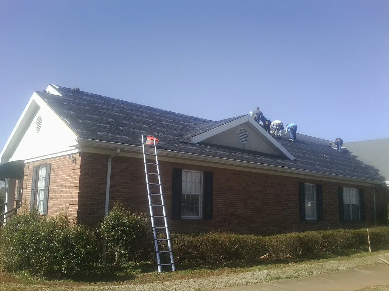 Crew tearing shingles off a brick ranch roof with a ladder set — Emergency Roof Repair work by our crew in Hillsborough