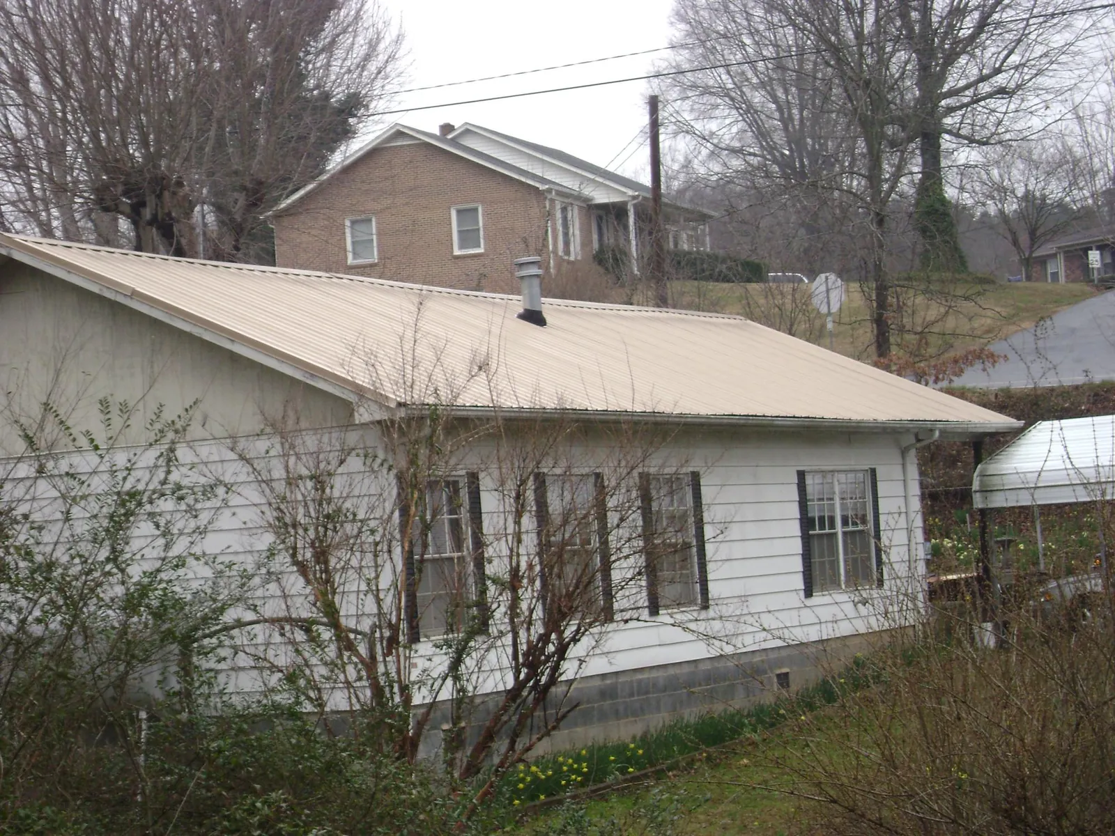 Tan metal roof on a white sided house set into a hillside — Commercial Roofing by Roofing Brothers in Hillsborough